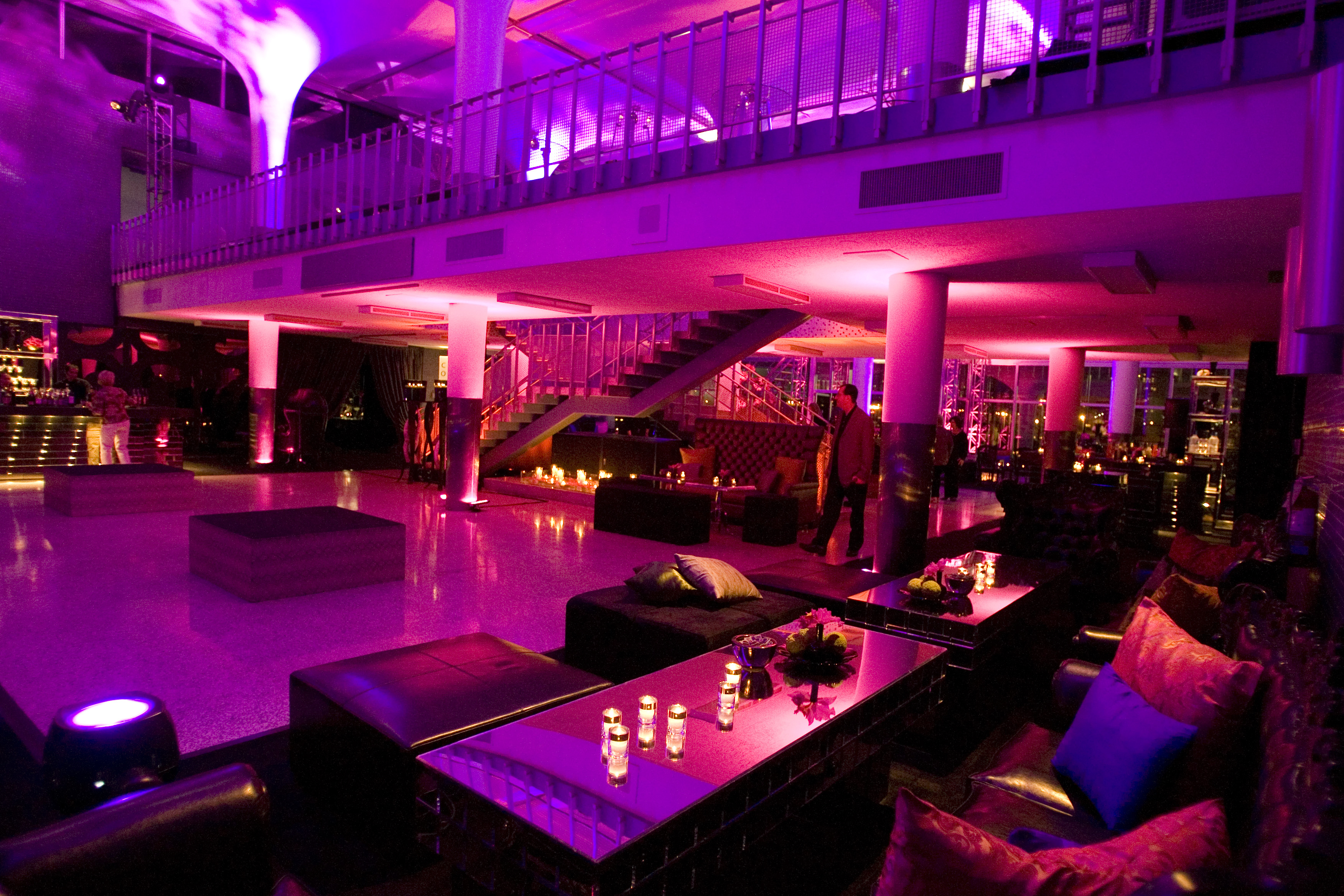 Large room bathed in pink light with seating areas, candles, and a bar.